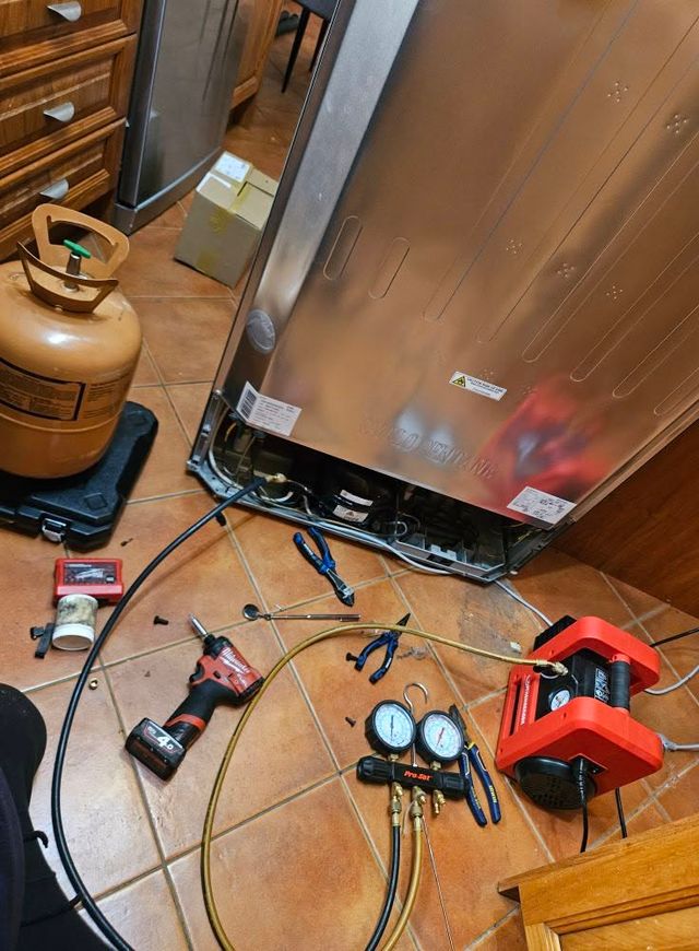 Manifold gauges, vacuum pump and refrigerant cylinder connected to a fridge during a re-gas in an Adelaide kitchen