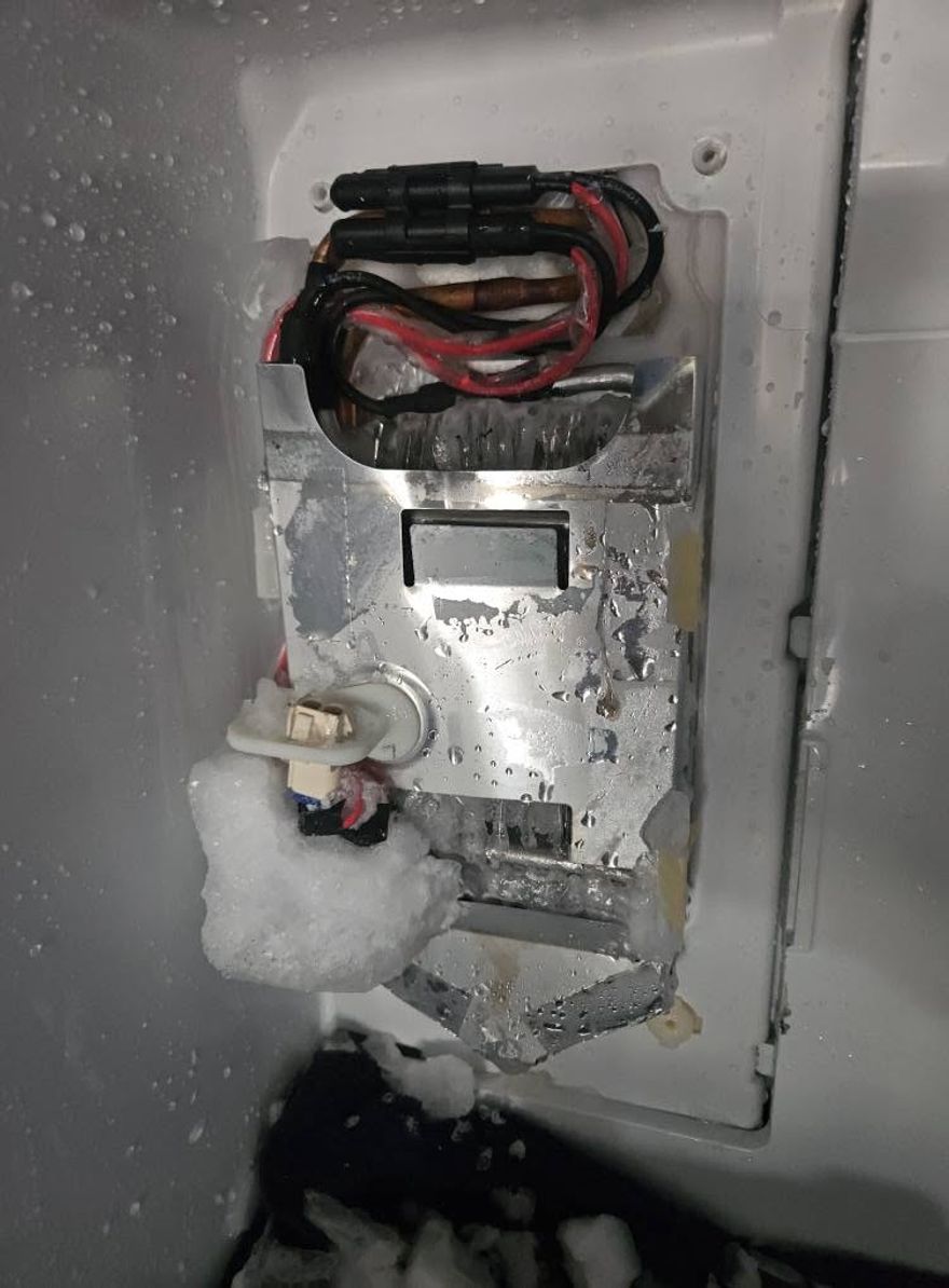Ice maker assembly caked in built up ice inside a freezer compartment during a repair