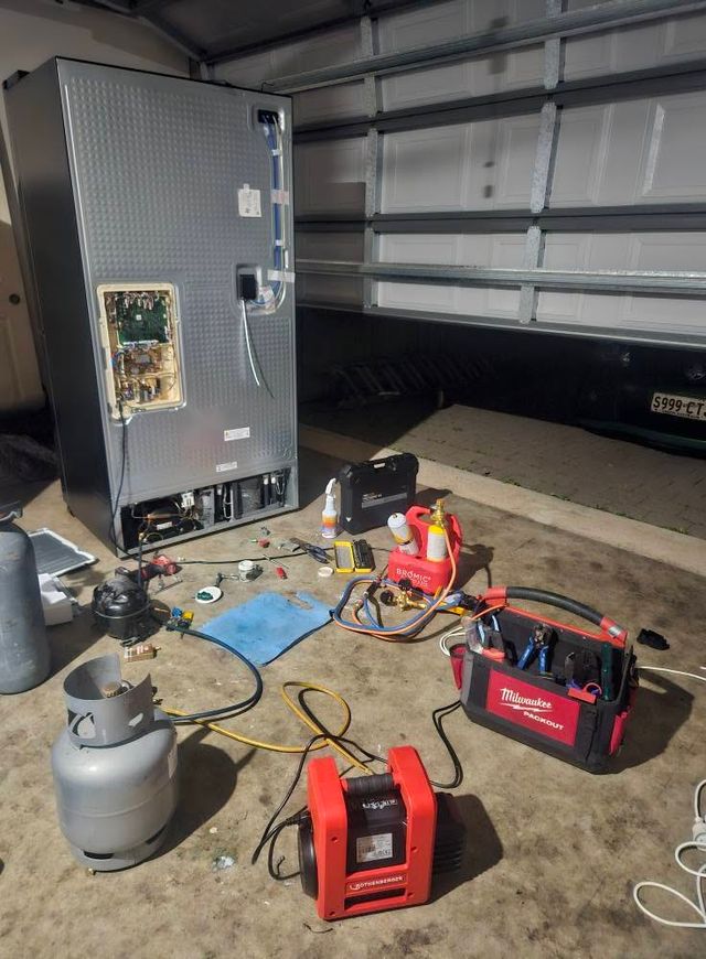 French door fridge with its rear panel removed, recovery unit, vacuum pump and refrigerant gear connected during a sealed system repair